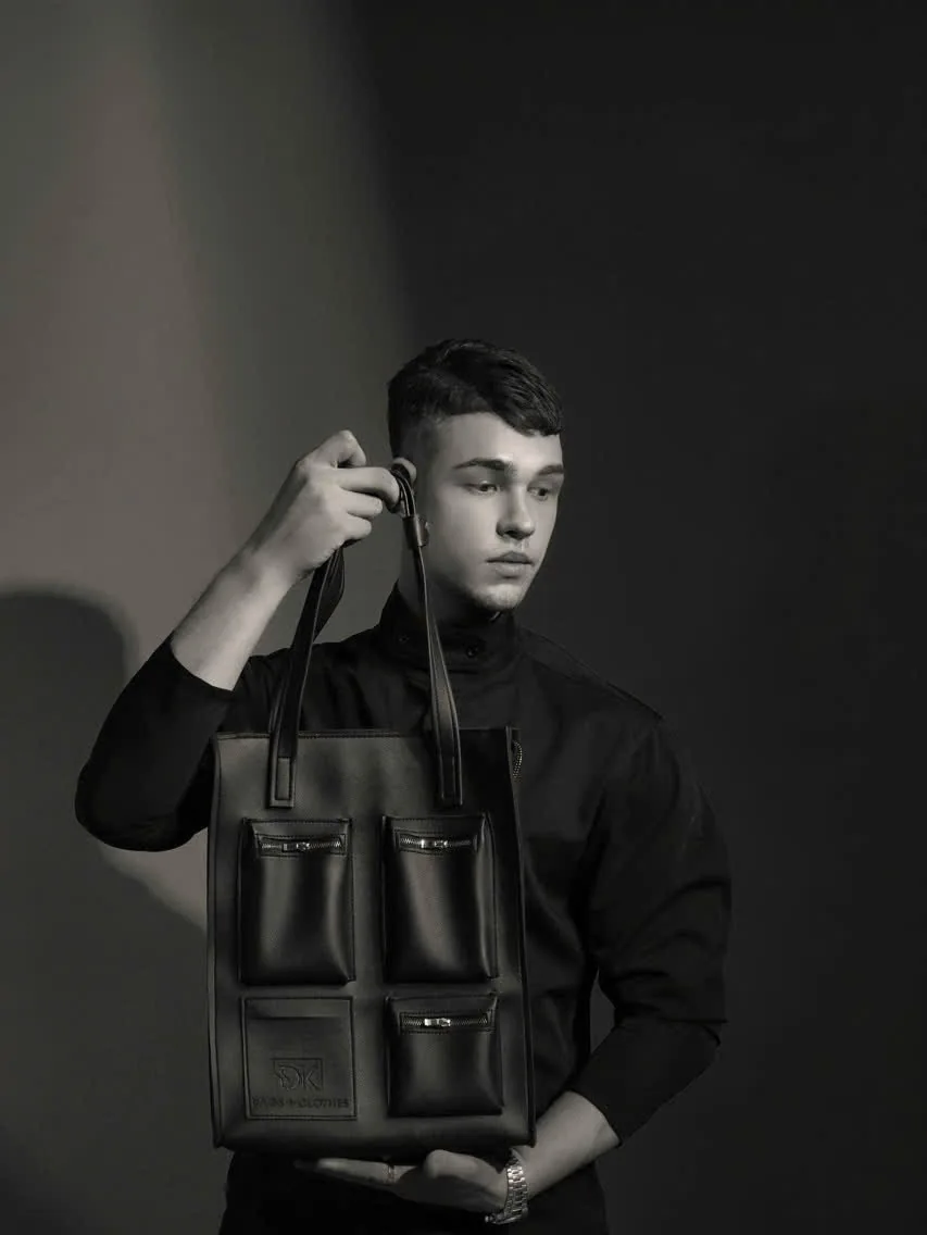 Black-and-white studio portrait: a model holds the DK 01 Moscow tote up by its handles, front pockets facing the camera.